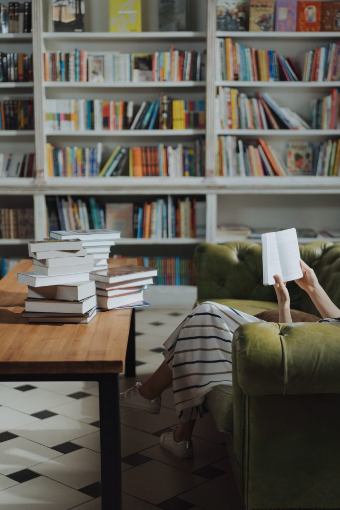 photo by cotton bro studio via Pexels woman reading a book whilst surrounded by more books
